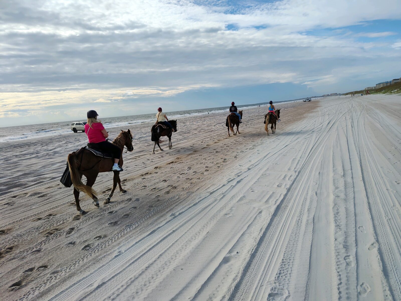group of people on horseback riding down the beach